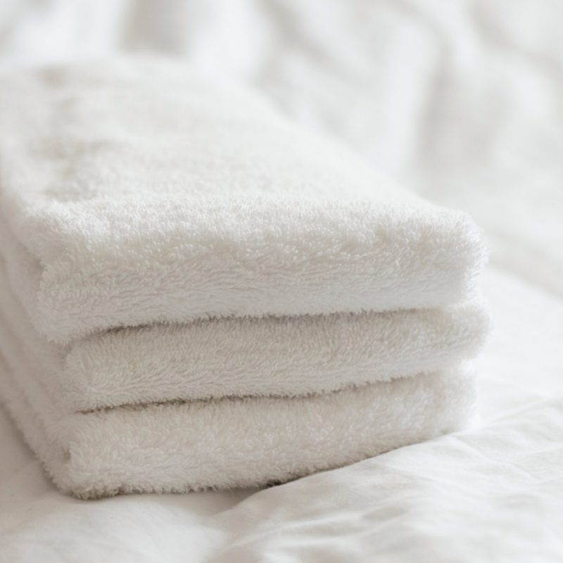 Freshly washed white hand towels stacked on a white bed.